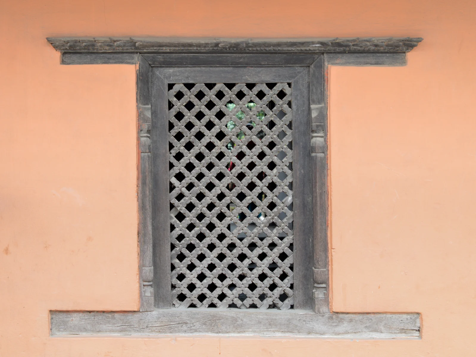 A wooden window grill set into a warm-colored wall in Pokhara.